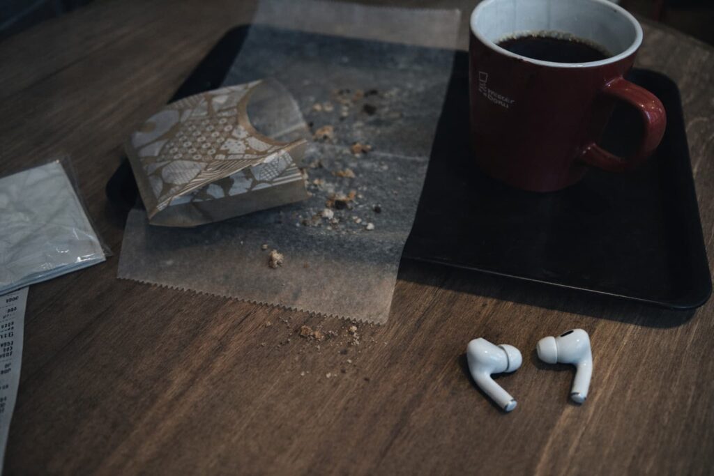 カフェのテーブルに残ったコーヒーの跡とイヤホン、食べ終えた後のパンくずが残る風景